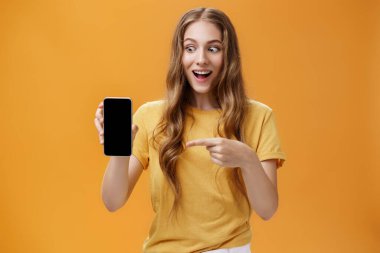 Heyecanlı bir kadının portresi elinde harika bir akıllı telefon tutarken cep telefonu ekranını işaret ederken hayran kalıyor. Havalı teknoloji ürünleri ile büyülenen cihaza deli gibi bakıyor.