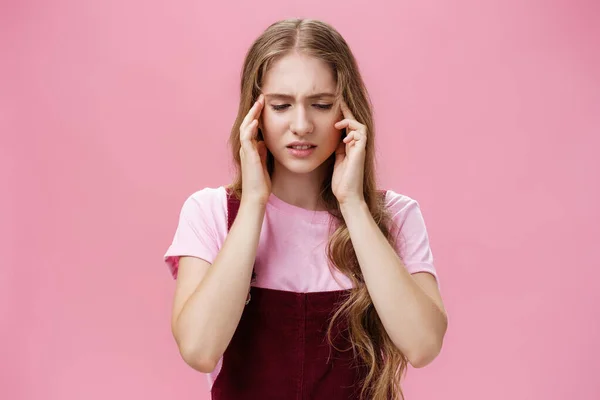 Femme ne peut pas se concentrer pendant le test ayant réponse glissé toucher les tempes regardant vers le bas préoccupé et troublé ayant mal à la tête ou des problèmes de mémoire debout mécontent sur le mur rose — Photo