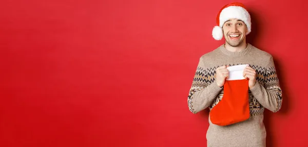 Concepto de vacaciones de invierno, año nuevo y celebración. Imagen del hombre sorprendido y feliz que recibe el regalo de santa secreta dentro de la bolsa de almacenamiento de Navidad, regalo abierto y buscando agradecido —  Fotos de Stock
