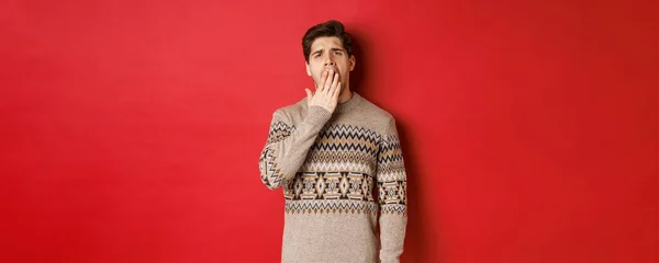 疲れや退屈ハンサムな男のイメージで冬のセーター、あくびや手で口をカバー、赤の背景に疲れ立って — ストック写真