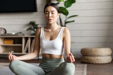 Farkındalık ve meditasyon kavramı. Genç Asyalı kadın evde egzersiz yapıyor. Oturma odasında yoga meditasyonu yapıyor.