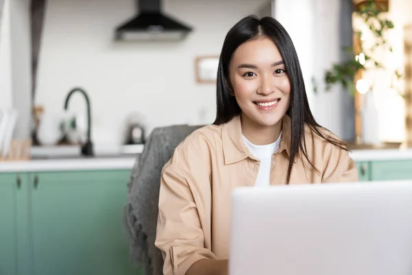 Sonriendo mujer asiática que trabaja desde casa con el ordenador portátil. Chica feliz usando la computadora para estudiar o trabajar, concepto de educación independiente y remota — Foto de Stock