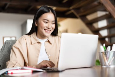 Gülümseyen Asyalı kız webinar sallıyor, evden iş videosu çekiyor, uzaktan serbest çalışıyor, bilgisayara mutlu bakıyor.