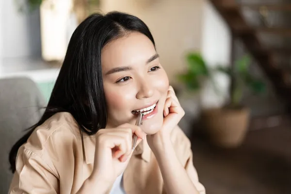 Портрет вдумливої азіатської дівчини, яка кусає ручку і посміхається, думає, шукає натхнення, робить домашнє завдання і стає творчою — стокове фото