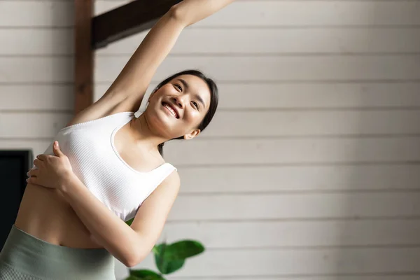 Esporte e estilo de vida conceito. Jovem asiática esportiva mulher com corpo apto alongamento corpo, levantando braços e flexão durante o treinamento de fitness em casa, vestindo activewear — Fotografia de Stock