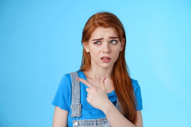 Aptal kızıl saçlı tereddütlü kız isteksiz, gönülsüz, tamamen inançsız, üründen emin olmayan, mavi arka planda duran garip adamdan hoşlanmayan,