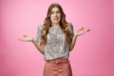 Garip, kafası karışık, çekici parti kızı omuz silkiyor, yüzünü buruşturuyor, farkında olmadan yüzünü buruşturuyor, belirsiz bir şekilde duruyor, özür diliyor, kazara çarpan araba, pembe arka plan.