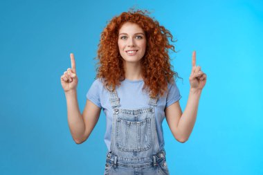 Motive olmuş neşeli kızıl saçlı aptal kıvırcık kadın işaret ediyor işaret parmağı gülümsüyor etkileyici bir şekilde harika tanıtım gösterisi yapıyor ilginç bir reklam hakkında konuşuyor mavi arka plan
