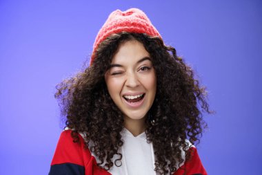 Çekici, sevimli bir kadın bizi davet ederek sevinçle kartopu oynamayı ima ediyor. Mavi arka planda poz veren şık kırmızı bereli ve kazaklı bir kadın.