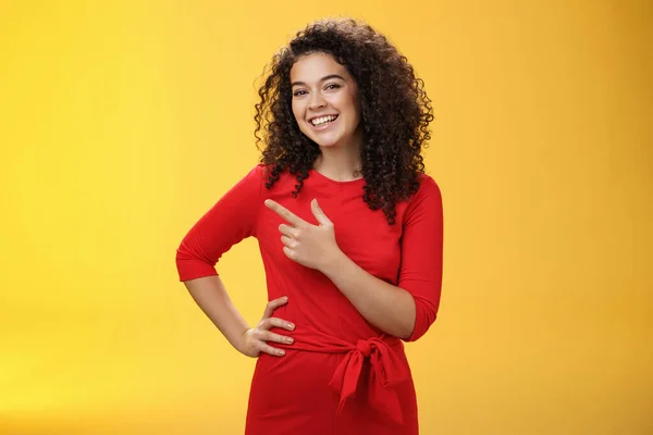 Portrait of friendly and assertive charming female coworker showing around newbie pointing left and smiling, laughing at camera having fun posing with hand on hip over yellow background — Stock Photo, Image