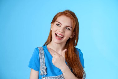 Şımarık, güzel, rüya gibi, kızıl saçlı kız öğrenci güzel bir performans sergiliyor, başını eğerek sola bakıyor, tatil planlarını tartışıyor, ilginç bir şekilde soru soruyor, mavi arka plan pozu veriyor.