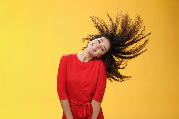 Fényes boldog és gondtalan játékos nő integetett göndör haj hullám és mosolyogva nagyjából, mint álló örömteli piros ruha sárga háttér jó hangulatban a jövőbeli kalandok — Stock Fotó