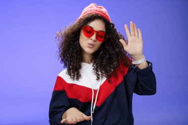 Kırmızı bereli ve güneş gözlüklü havalı ve şık bir DJ kızın stüdyo çekimi. Havalı müzik eşliğinde palmiye yükselterek dans etmek ve ritim tutarak dans etmek. Harika bir partide mavi duvarın üzerinde ürperti pozu vermek.