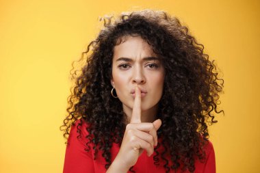 Tek kelime etme. Ciddi görünümlü, kıvırcık saçlı, sessiz jest gösteren, katlanmış dudakları işaret parmağıyla kaşlarını çatan, gizli bir söz veren ve sarı duvarın üzerinde sessiz kalan genç bir kadının portresi.