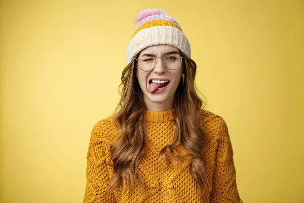 Despreocupado atractivo divertido feliz chica caucásica de 20 años pelo rizado gafas sombrero suéter divertirse juguetonamente mostrar la lengua, guiño coqueta expresar estado de ánimo optimista positivo, fondo amarillo —  Fotos de Stock