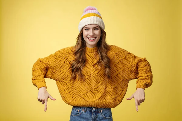 Friendly-looking helpful όμορφος 20s κολέγιο κορίτσι φοιτητής φορώντας καπέλο ζεστό πουλόβερ χαμογελώντας στην ευχάριστη θέση να σας δείξει φοβερό προαγωγή δείχνοντας δείκτες προς τα κάτω προτείνουμε κάτω διαφήμιση — Φωτογραφία Αρχείου