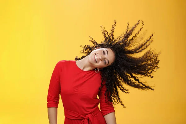 Menina ficando despreocupado e selvagem acenando cabelo e fazendo sol com cachos voando no ar sorrindo amplamente inclinando a cabeça e se divertindo, dançando encantado e divertido sentindo-se brincalhão contra o fundo amarelo — Fotografia de Stock