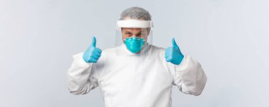 Covid-19, virüsü önleme, sağlık çalışanları ve aşı konsepti. Korunma ekipmanları içinde kendine güvenen bir doktor var. Baş parmağını kaldır ve her şeyin yolunda olduğuna emin ol.