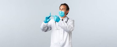 Covid-19, virüsü önleme, sağlık çalışanları ve aşı konsepti. Tıbbi maskeli orta yaşlı bir doktor ve elinde Coronavirus aşısı ya da HIV aşısı olan bir şırınga tutan eldivenler var.