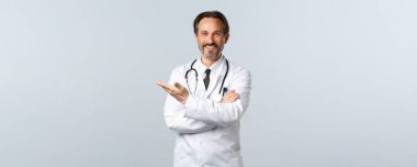 Covid-19, koronavirüs salgını, sağlık çalışanları ve pandemik konsept. Yakışıklı dost canlısı doktor yolu gösteriyor. Beyaz önlüklü doktor tanıtımda sol elini göstererek hastaları davet ediyor.