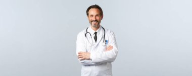 Covid-19, koronavirüs salgını, sağlık çalışanları ve pandemik konsept. Hevesli gülümseyen doktor, beyaz önlüklü doktor hevesli görünüyor, kollarını kavuşturup hastayı dinliyor.