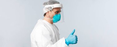 Covid-19, virüsü önleme, sağlık çalışanları ve aşı konsepti. Şahsi koruyucu ekipmanlı neşeli doktor profili baş parmak yukarı hastayı gösteriyor, her şeyin yolunda olduğundan emin olun, endişelenmeyin.