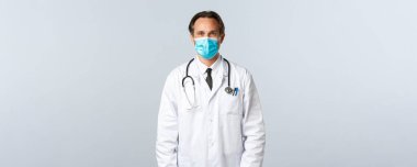 Covid-19, virüsü önleme, sağlık çalışanları ve aşı konsepti. Beyaz önlüklü ve tıbbi maskeli orta yaşlı profesyonel terapist klinikteki hastayı dinliyor, doktorluk yapıyor.