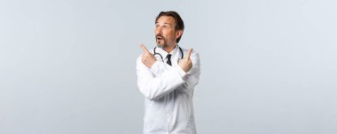 Covid-19, koronavirüs salgını, sağlık çalışanları ve pandemik konsept. Beyaz önlüklü kararsız doktor, parmaklarını yana doğru gösteriyor ve değişkenlere bakıyor, seçim yapıyor.