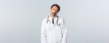 Covid-19, koronavirüs salgını, sağlık çalışanları ve pandemik konsept. İsteksiz tedirgin, kasvetli doktor iç çekiyor ve rüya gibi, görüntüleme tatile gitmek istiyor, gece vardiyası yapıyor.