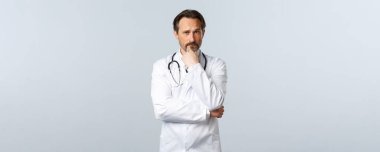 Covid-19, koronavirüs salgını, sağlık çalışanları ve pandemik konsept. Düşünceli ciddi bir doktor karar veriyor, hasta vakasına odaklanmış gibi görünüyor. Hekim varsayımda bulunuyor