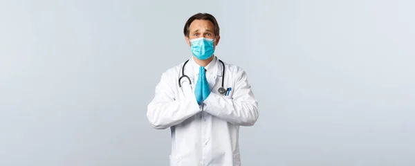 Covid-19, virüsü önleme, sağlık çalışanları ve aşı konsepti. Umut dolu, tıbbi maskeli ve eldivenli doktor. Dua ederken, kaşlarını çatarken, iyilik isterken. — Stok fotoğraf