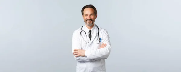 Covid-19, Coronavirus-Ausbruch, Gesundheitspersonal und Pandemiekonzept. Enthusiastisch lächelnder Arzt, Arzt im weißen Mantel, der enthusiastisch guckt, Brustkorb verschränkt, Patient zuhört — Stockfoto