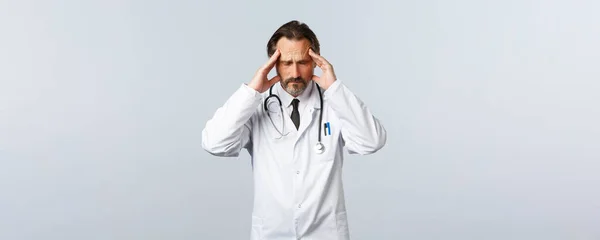 Covid-19, surto de coronavírus, profissionais de saúde e conceito de pandemia. Médico perturbado ou exausto que luta contra doenças clínica, com dor de cabeça ou enxaqueca, dor de cabeça — Fotografia de Stock