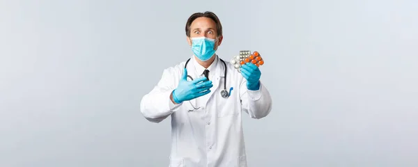 Covid-19, πρόληψη του ιού, εργαζόμενοι στον τομέα της υγείας και την έννοια του εμβολιασμού. Ενθουσιασμένος και σοκαρισμένος γιατρός με ιατρική μάσκα και γάντια αντιδρούν σε νέα φάρμακα, δείχνοντας χάπια, λευκό φόντο — Φωτογραφία Αρχείου