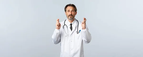 Covid-19, ξέσπασμα του ιού της στέψης, επαγγελματίες υγείας και πανδημία. Ελπίδα ανήσυχος αρσενικό γιατρό εκλιπαρεί απελπισμένος, σταυρώνουν τα δάχτυλα καλή τύχη, κάνοντας ευχή ως αίσθημα ανησυχίας — Φωτογραφία Αρχείου