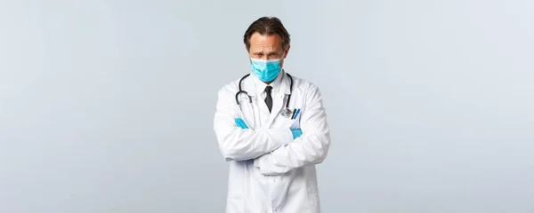 Covid-19: 바이러스 예방, 의료 종사자 및 예방 개념. 의료용 마스크와 장갑을 착용하고 모욕적 이고 불쾌 해 보이는 소심 한 의사, 손의 가슴을 교차하고 우울 한 인상을 주는 — 스톡 사진