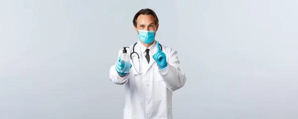 Covid-19, πρόληψη του ιού, εργαζόμενοι στον τομέα της υγείας και την έννοια του εμβολιασμού. Ενθουσιαστικός χαμογελαστός γιατρός εξηγεί τη σημασία της χρήσης απολυμαντικό χεριών, δείχνουν τον κανόνα νούμερο ένα, φορούν ιατρική μάσκα και γάντια — Φωτογραφία Αρχείου