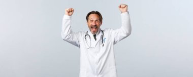 Covid-19, koronavirüs salgını, sağlık çalışanları ve pandemik konsept. Rahatlamış erkek doktor tezahürat yapıyor, evet diyor ve yumruk tokuşturarak iyi haberi kutluyor, galibiyeti yeniyor.