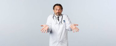Covid-19, koronavirüs salgını, sağlık çalışanları ve pandemik konsept. Kafası karışmış erkek doktor, garsonlara boş eller göstererek ve omuz silkerek bir hata yaptı.