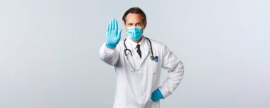 Covid-19, virüsü önleme, sağlık çalışanları ve aşı konsepti. Tıbbi maskeli ve eldivenli ciddi bir doktor, sosyal mesafeyi engellemek, engellemek, reddetmek veya kısıtlamak için ellerini uzatır.