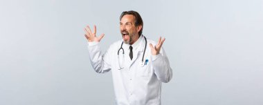 Covid-19, koronavirüs salgını, sağlık çalışanları ve pandemik konsept. Beyaz önlüklü deli doktor, klinikte çalışanla yüzleşiyor, kızgın hareketler yapıyor ve öfkeli görünüyor.