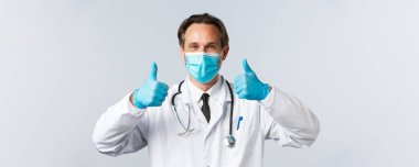 Covid-19, virüsü önleme, sağlık çalışanları ve aşı konsepti. Tıbbi maske ve eldiven takmış orta yaşlı doktorların yakın plan çekimleri, onaylama için onay verin ve ürün önerin.