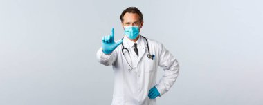 Covid-19, virüsü önleme, sağlık çalışanları ve aşı konsepti. Tıbbi maskeli ve eldivenli ciddi bir doktor. Parmaklarını sallıyor, azarlıyor, koronavirüslü hastaları yasaklıyor ya da uyarıyordu.