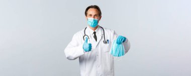 Covid-19, virüsü önleme, sağlık çalışanları ve aşı konsepti. Tıbbi maskeli tatmin olmuş doktor ve eldivenler PPE 'yi tavsiye ediyor. Maskelerin kalitesinin garantisi olarak başparmağınızı kaldırın.