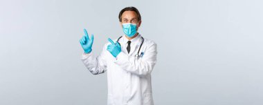 Covid-19, virüsü önleme, sağlık çalışanları ve aşı konsepti. Beyaz önlüklü, tıbbi maskeli ve eldivenli şaşırmış doktor sol üst köşeyi işaret ediyor.