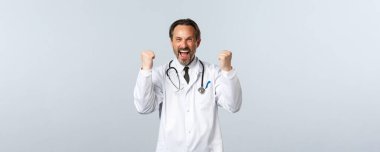 Covid-19, koronavirüs salgını, sağlık çalışanları ve pandemik konsept. Heyecanlı erkek doktor kazanıyor, iyi haberler alıyor, yumruk tokuşturarak ilahi söylüyor, evet seviniyor, başarıyı kutluyor.