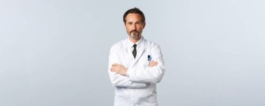 Beyaz önlüklü, kolları çapraz göğüslü ciddi görünümlü bir doktor, kendinden emin görünüyor. Hastanedeki hastaları tedavi etmek. Klinikteki doktor covid-19 'u test ediyor, hastalara ilaç yazıyor.