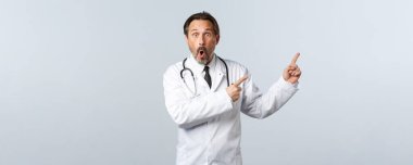 Covid-19, koronavirüs salgını, sağlık çalışanları ve pandemik konsept. Şaşırmış ve etkilenmiş beyaz önlüklü doktor sağ üst köşeyi işaret ediyor, çenesini indir ve reklamda vay canına de.