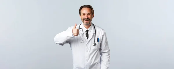 Covid-19, ξέσπασμα του ιού της στέψης, επαγγελματίες υγείας και πανδημία. Όμορφος χαρούμενος αρσενικό γιατρό σε λευκό παλτό δείχνουν αντίχειρες-up στην έγκριση, συμφωνούν ή σαν προϊόν, συνιστώντας — Φωτογραφία Αρχείου