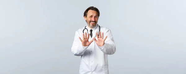 Covid-19, coronavirus outbreak, healthcare workers and pandemic concept. Displeased and bothered doctor rejecting something awful, shaking hands in refusal or denial, look alarmed — Stock Photo, Image